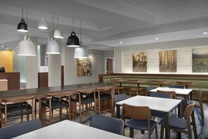 Un intérieur de restaurant moderne avec un long comptoir, de nombreux types de sièges et des luminaires suspendus.