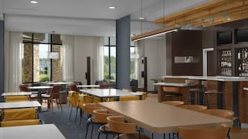 Un comedor moderno con varias mesas y sillas, una zona de bar con mostrador y taburetes, y ventanas amplias que ofrecen luz natural.