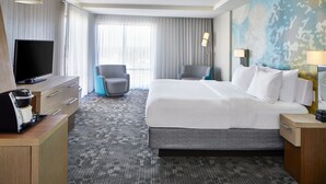 Habitación de hotel con una cama grande, un televisor de pantalla plana, un escritorio con cafetera y vistas al exterior por la ventana.