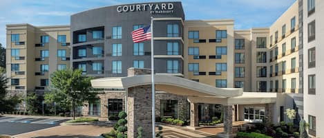 A Courtyard by Marriott hotel with a modern design, featuring a prominent American flag, a covered entrance, and a landscaped courtyard.