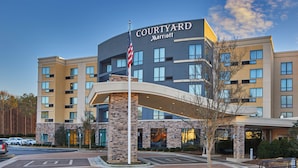 Un hotel Courtyard Marriott con diseño moderno, que presenta una bandera estadounidense destacada, un acceso cubierto y un área de estacionamiento.