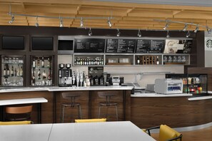 Eine moderne Bar mit verschiedenen Sitzmöglichkeiten, einer Kaffeemaschine und einer Auswahl an Getränken und Snacks.