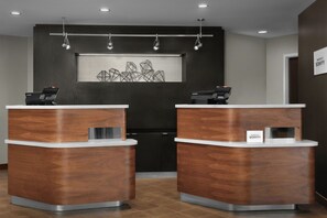A reception area with two wooden reception desks, a wall-mounted artwork, and a sign indicating the hotel name. - Courtyard by Marriott Atlanta Lithia Springs (Lithia Springs)