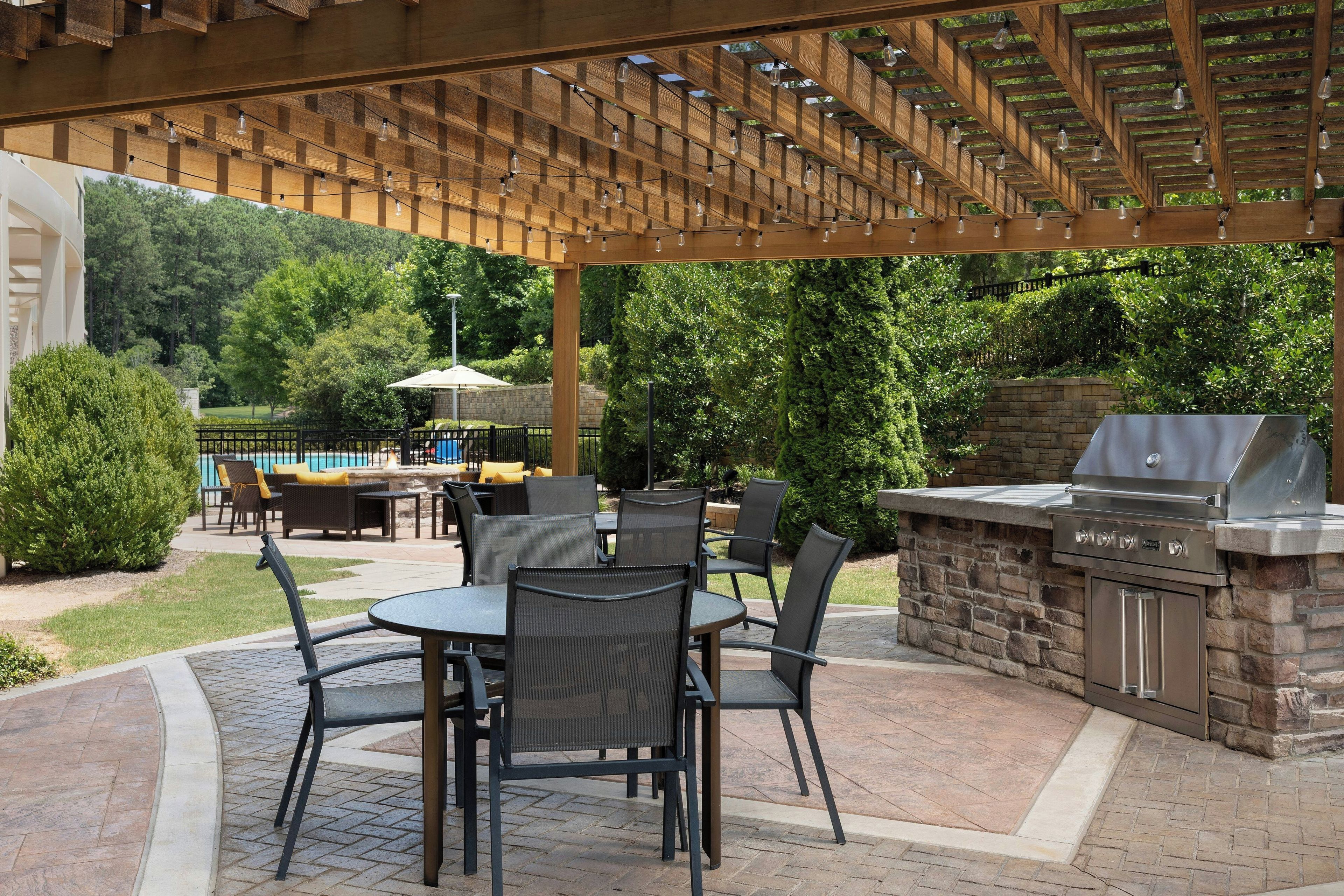 An outdoor patio with a pergola, dining area, and a barbecue grill.