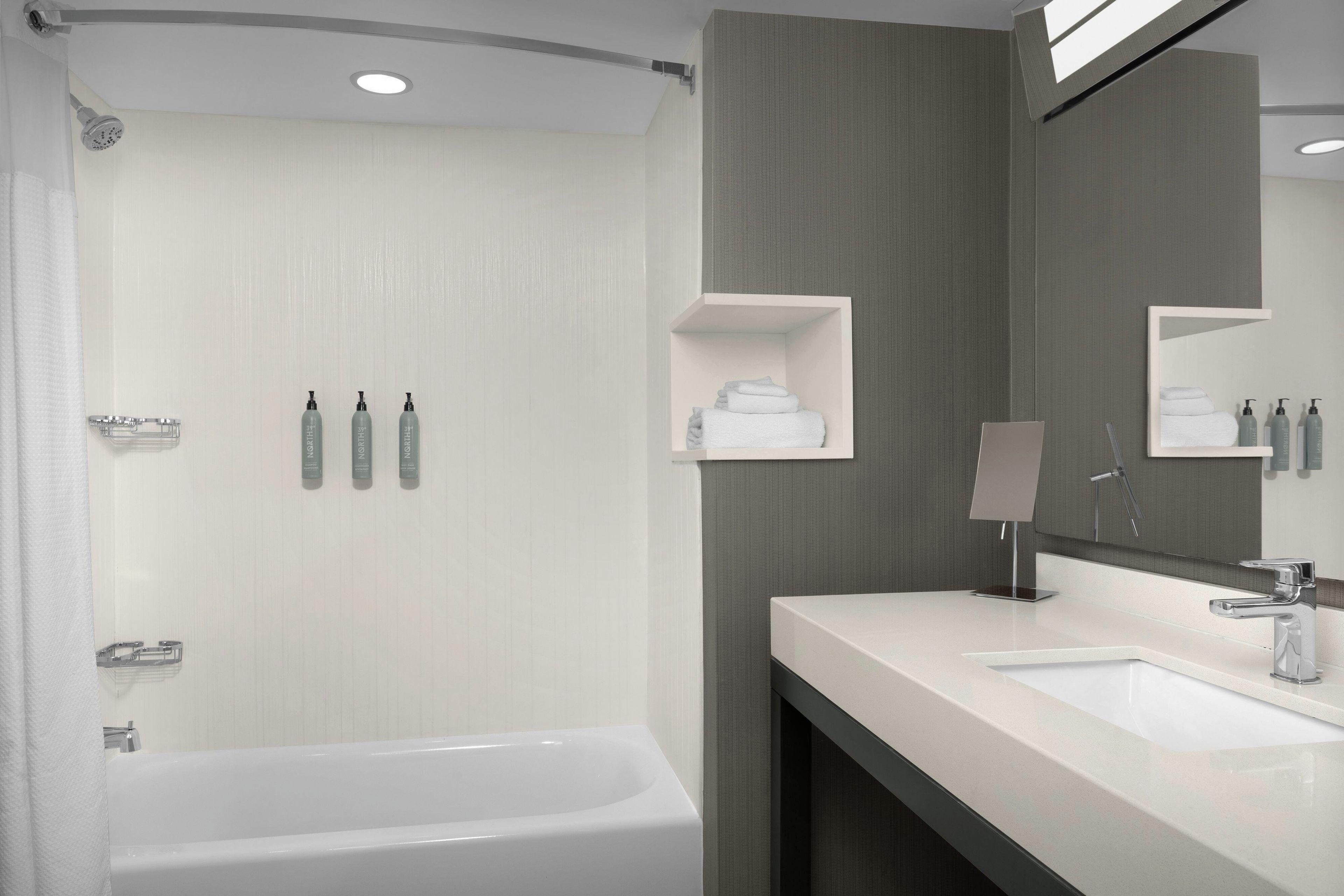A modern bathroom with a bathtub, a vanity with a mirror, and toiletries on the wall.
