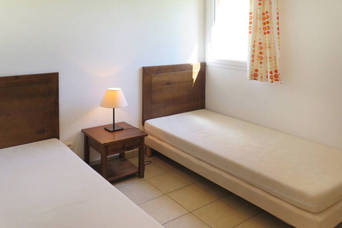 Ein kleines, sauberes Zimmer mit zwei Betten, einem Nachttisch und einer Lampe.