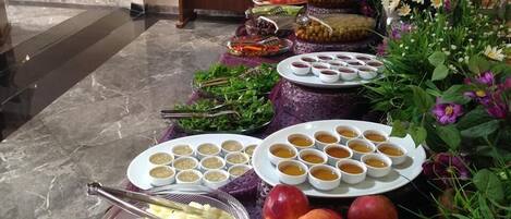 Una mesa de bufé con diversos alimentos, como platos de manzanas, tazones de sopa y recipientes con aceitunas.