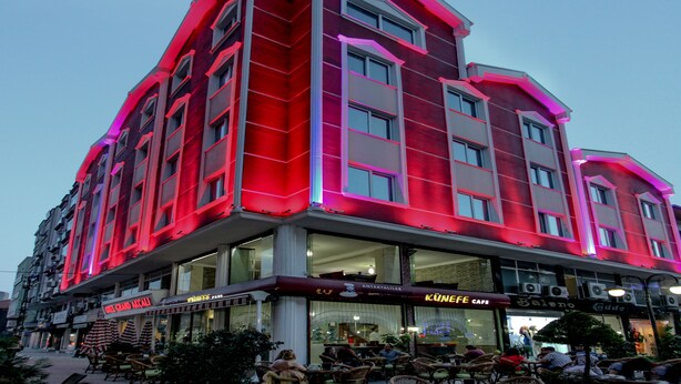 Un immeuble à plusieurs étages doté d’une façade rouge et rose remarquable, avec de grandes fenêtres et un café situé au rez-de-chaussée.