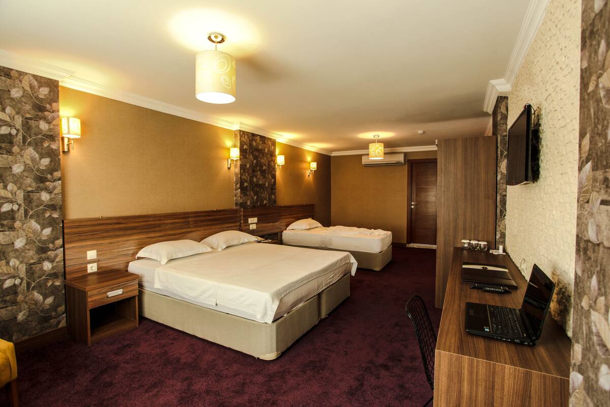 A hotel room with a large bed, a desk with a laptop, and a TV on the wall.