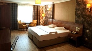 Une chambre d’hôtel avec un grand lit, un bureau avec un téléphone, deux chaises, une petite table et une fenêtre avec des rideaux.
