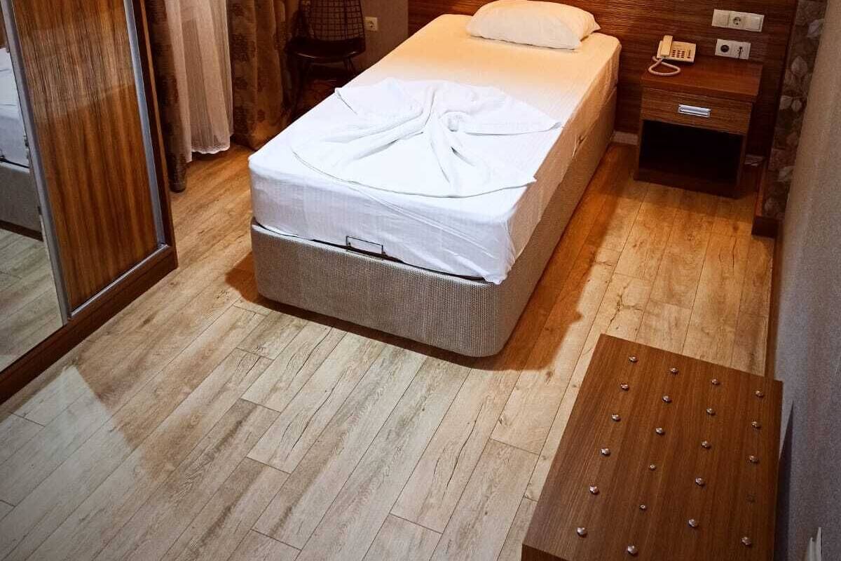 A hotel room with a bed, a wooden nightstand, a telephone, a lamp, a mirror, and a wardrobe.
