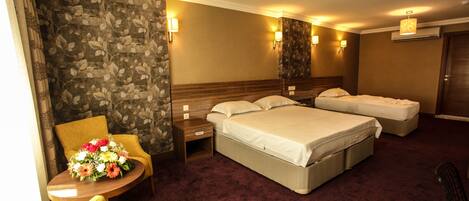 A hotel room with a large bed, two bedside tables, a chair, a small round table with a floral arrangement, and a carpeted floor.