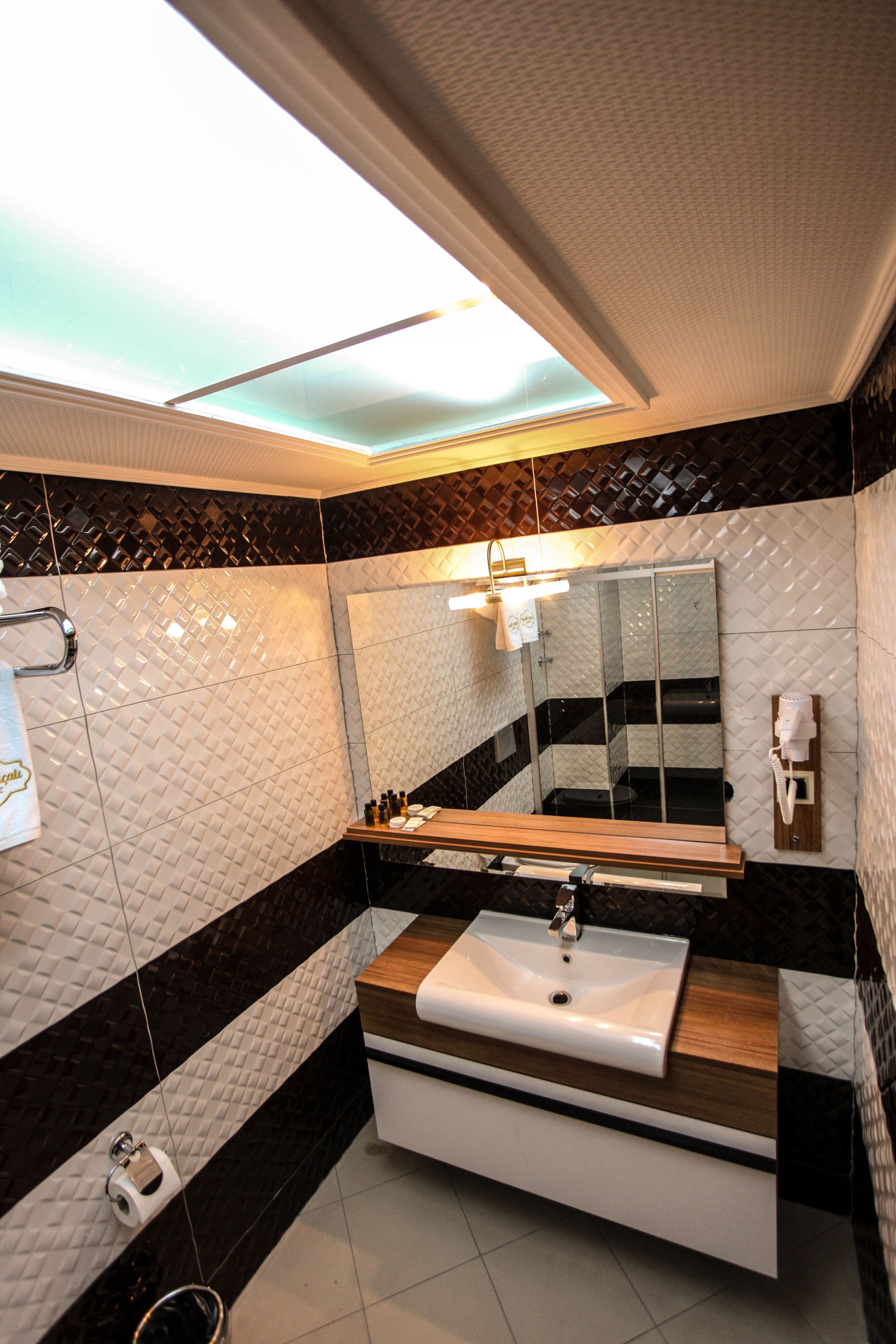 A modern bathroom with a skylight, a large mirror, a sink, and a toilet.