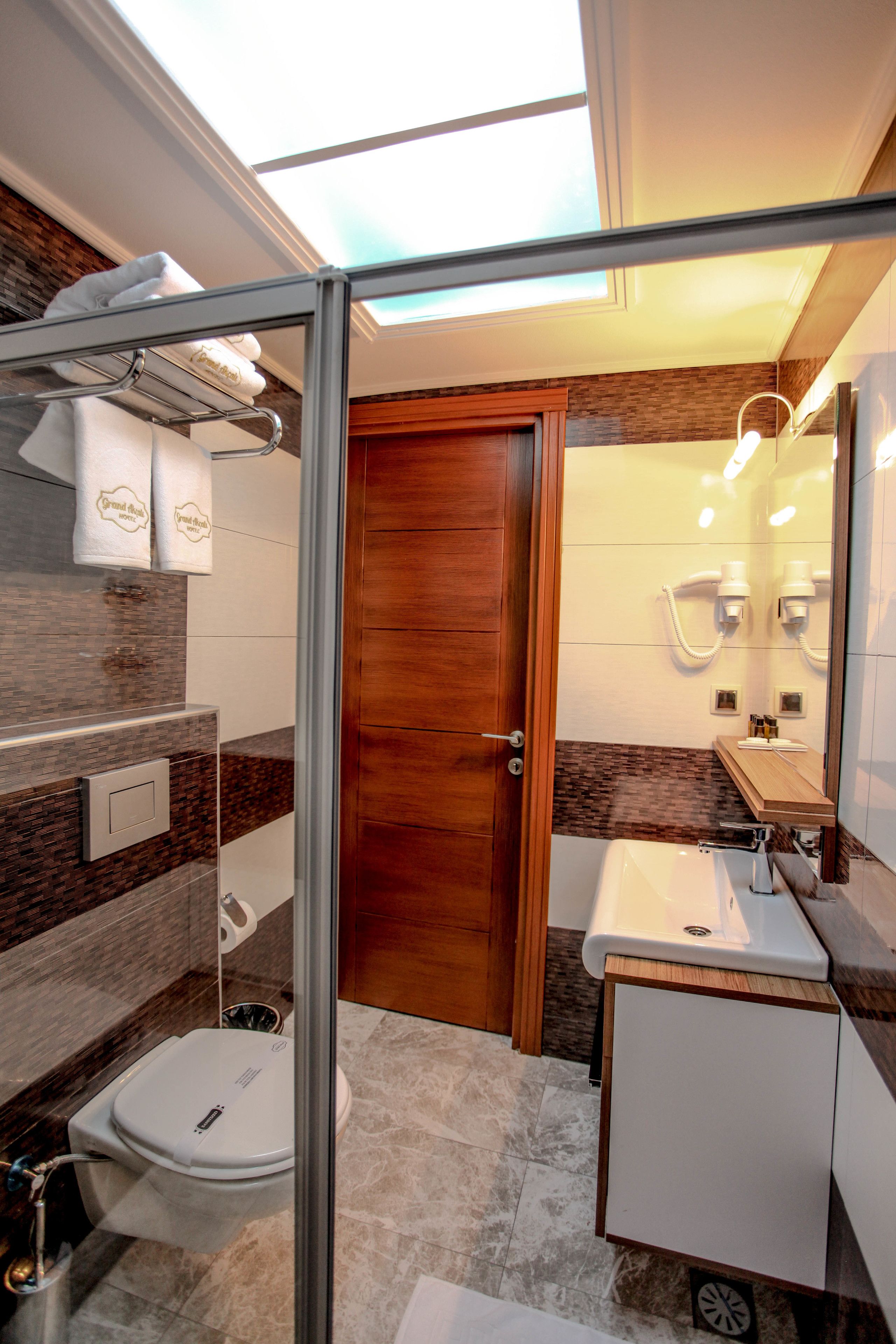 A modern bathroom with a glass shower enclosure, a wooden door, a white toilet, and a vanity with a mirror.