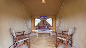 Una carpa con una mesa central y dos sillas, una lámpara colgante y vistas por la entrada.