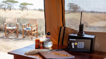 A wooden table with a knife, a bottle, and a safe in a safari tent.