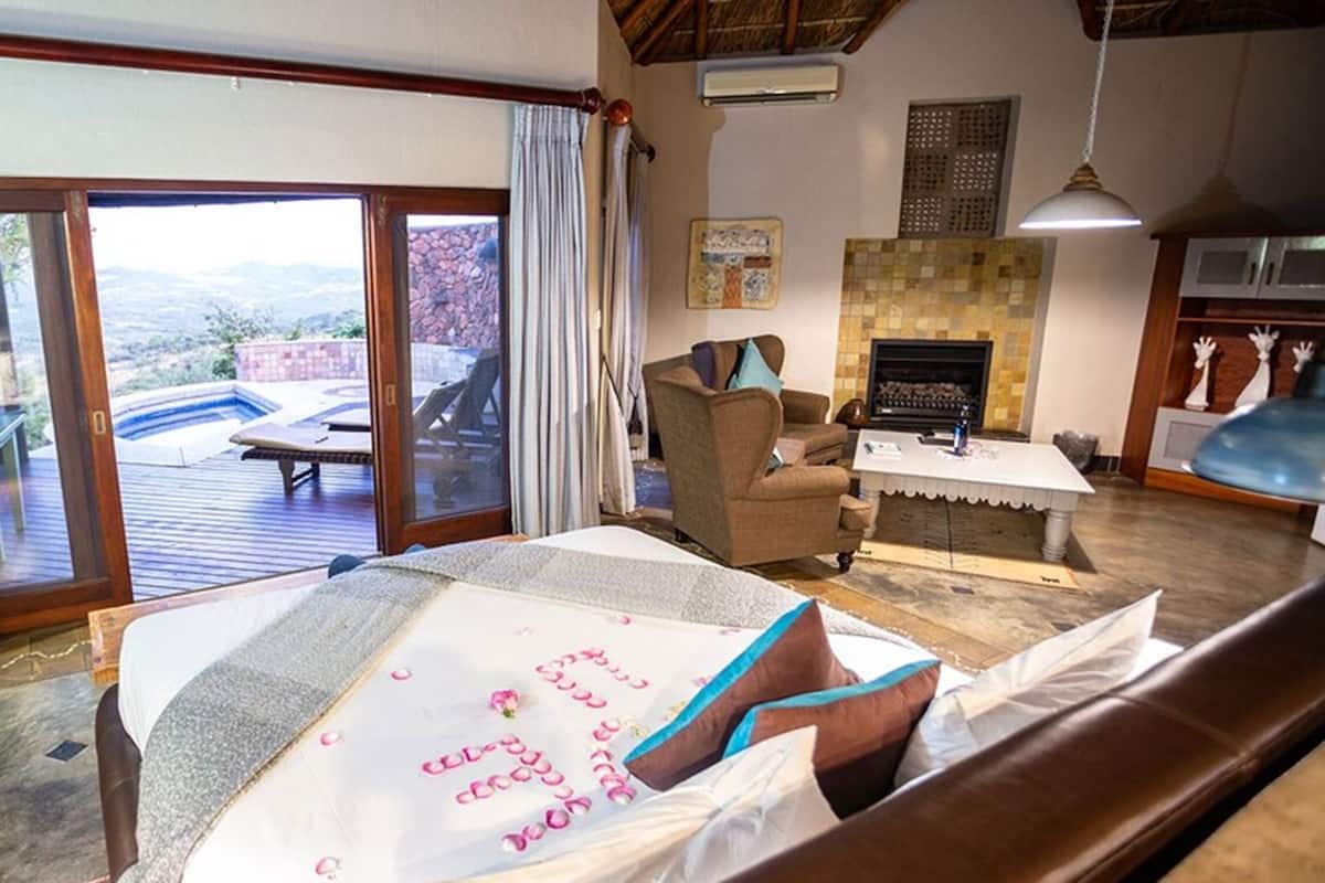 Een slaapkamer met een grote schuifpui naar een terras, een open haard en een eethoek met een tafel en stoelen.