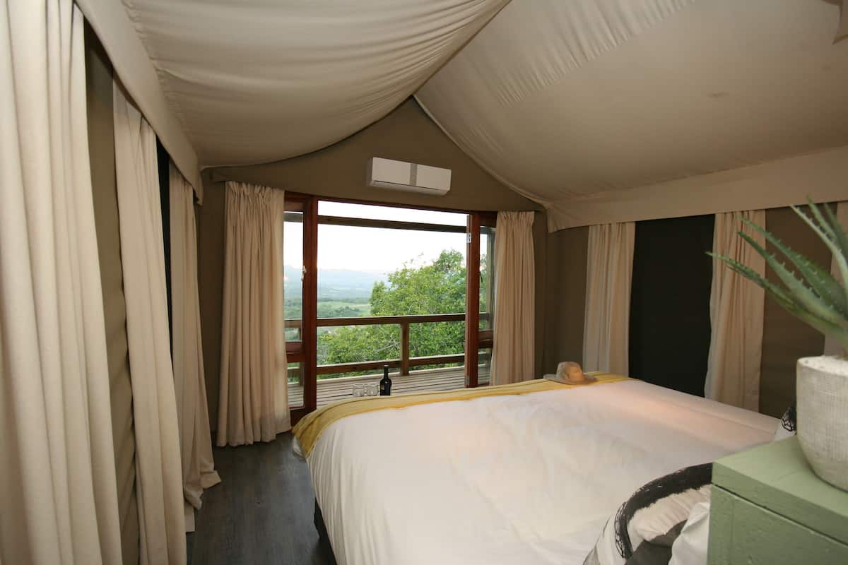 Een slaapkamer met een groot bed, een houten hoofdbord, een nachtkastje en uitzicht op het landschap.