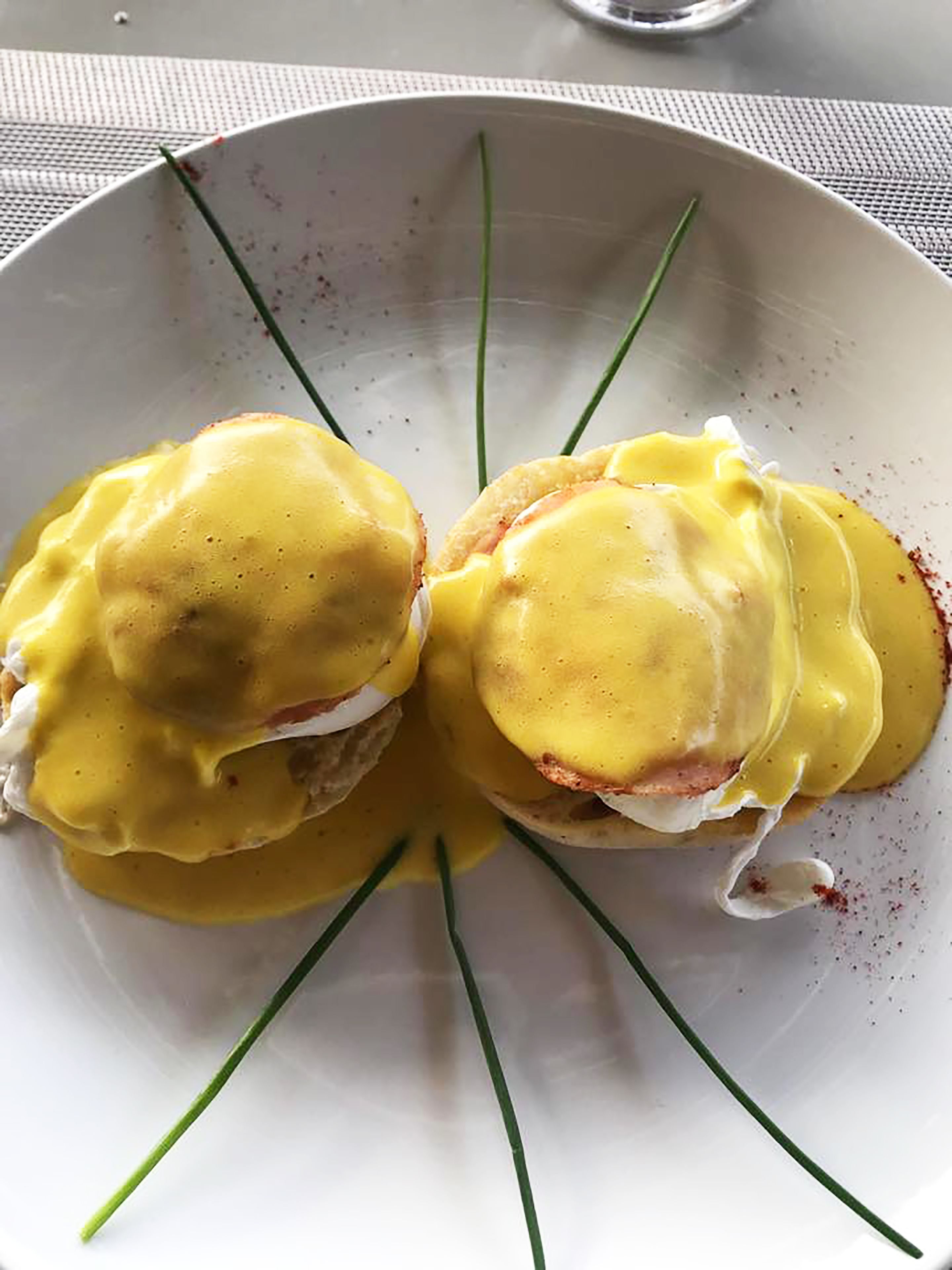 Deux œufs Bénédicte servis sur une assiette blanche, garnis de ciboulette.
