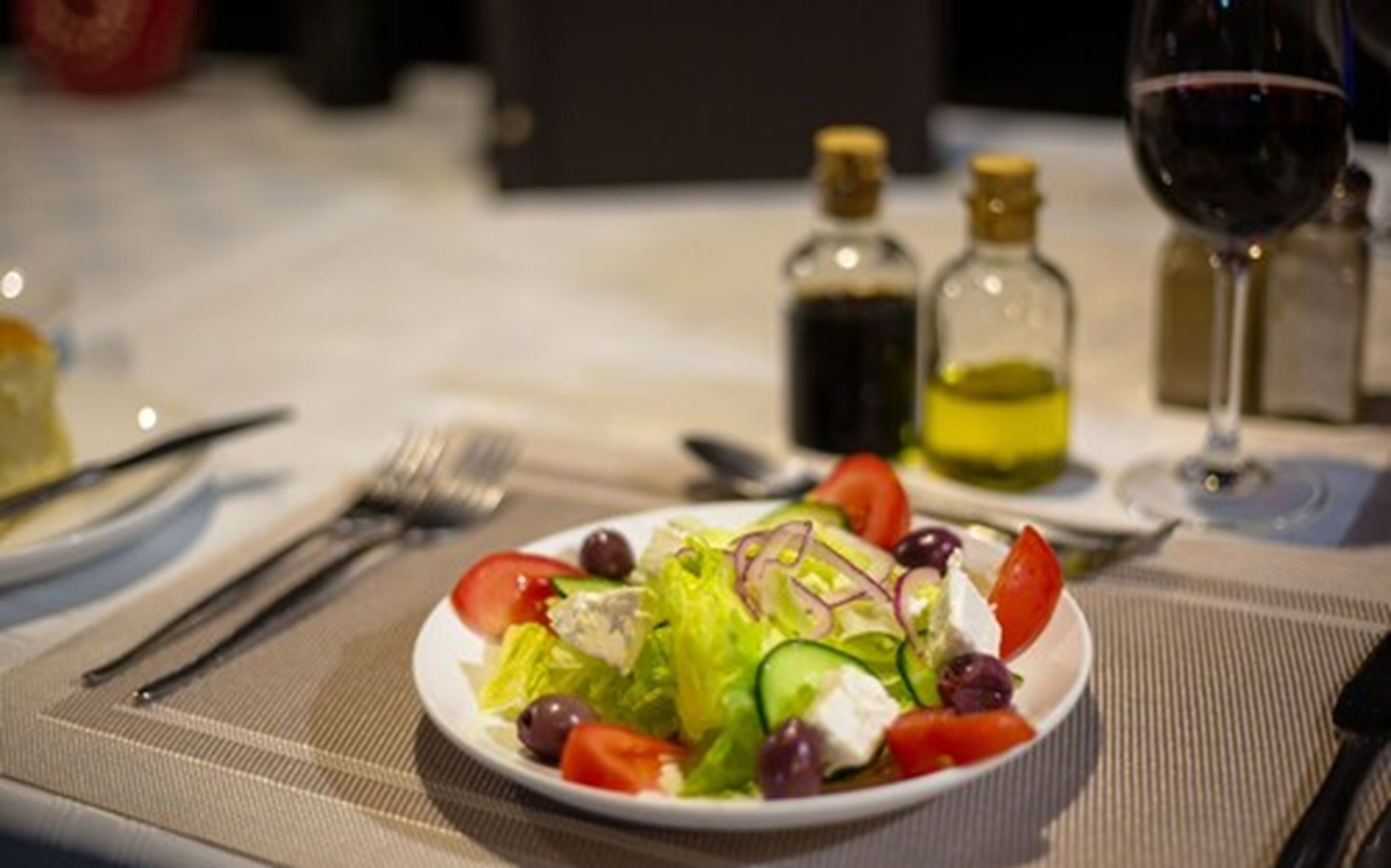 A plate of salad with various vegetables and a glass of red wine on a table.