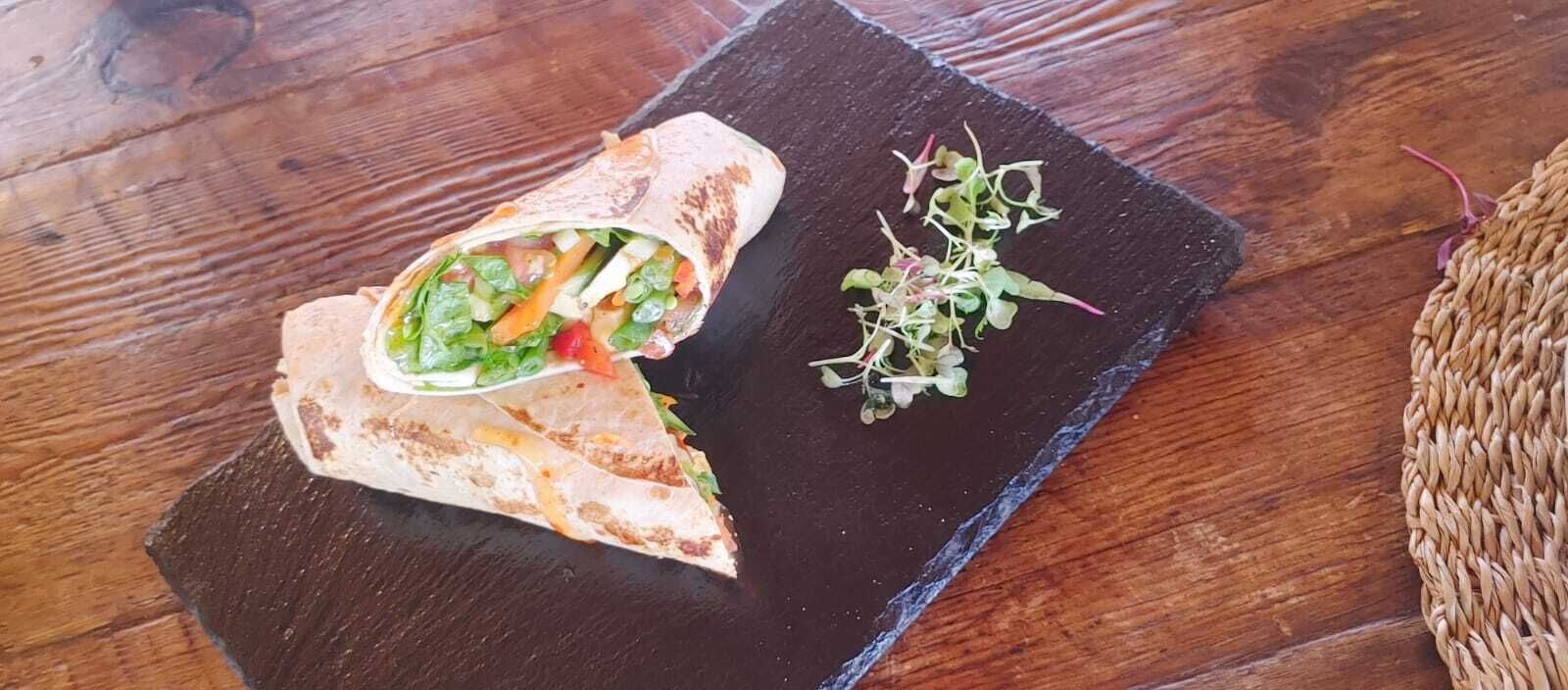 A wrap with vegetables on a dark slate plate.