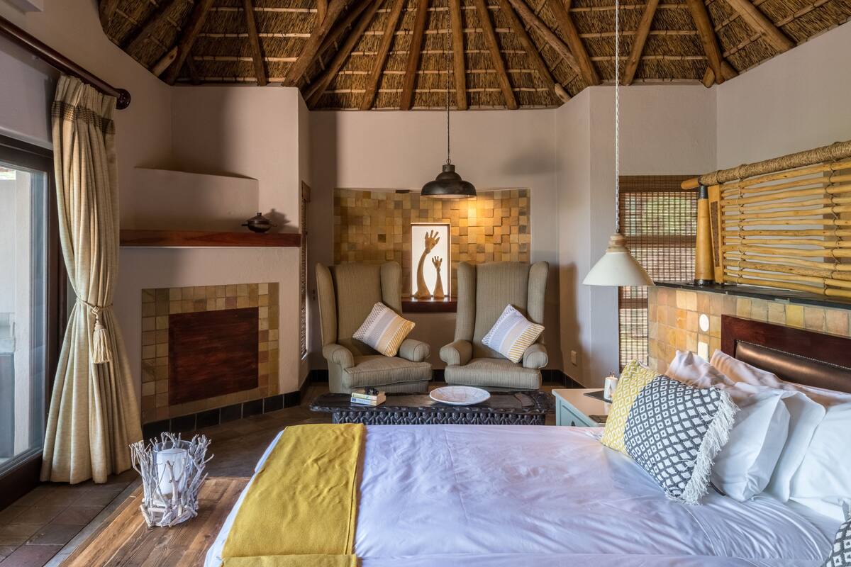 Een kamer met een bed, twee fauteuils, een open haard en een rieten plafond.