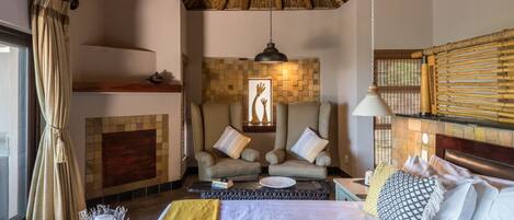 A room with a bed, two armchairs, a fireplace, and a thatched ceiling.
