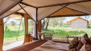 A tented room with a bed, a table, and a chair. - Gnu Ndutu Camp (Ngorongoro)
