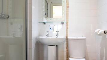 A bathroom with a glass shower enclosure, a pedestal sink, a toilet, and a mirror with a decorative tile border.