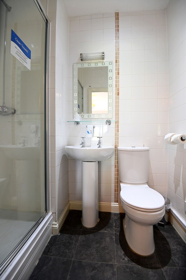 A bathroom with a glass shower enclosure, a pedestal sink, a toilet, and a mirror with a decorative tile border. - Admiral's Table, Bridgwater by Marston's Inns (Bridgwater)