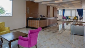 A hotel lobby with a reception desk, seating area, and large windows.