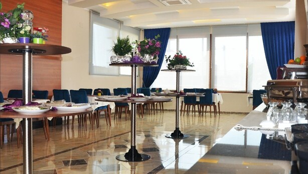 A hotel dining area with multiple tables and chairs, a buffet station, and decorative plants.