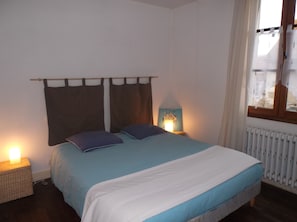 A bedroom with a bed, two bedside lamps, a nightstand, a window with curtains, and a radiator. - Le Pigeonnier Chambres d'hotes (La Roche-Posay)