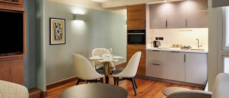 A modern living room with a round table and chairs, a sofa, and a kitchen area with cabinets and appliances.