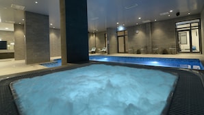 Un área interior de piscina moderna con un jacuzzi, sillones de descanso y una mesa de recepción.