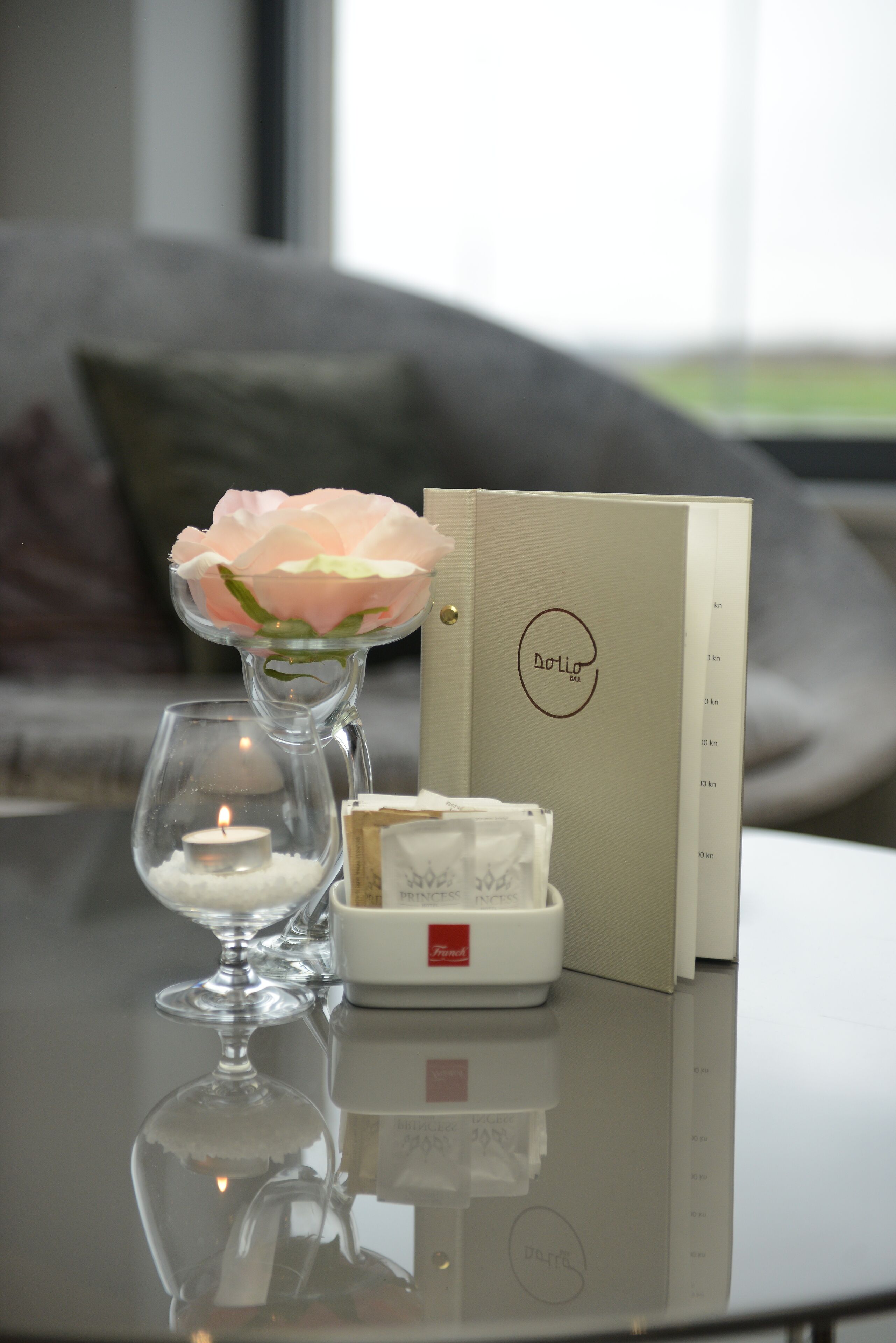 A table with a glass candle holder, a candle, a small white box, and a card with the text "Dolio Spa".