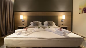 Una cama bien tendida con sábanas y toallas blancas, dos lámparas de noche y un cabecero de madera.