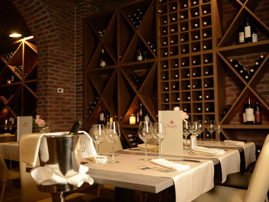 Un restaurante con pared de ladrillo y estanterías para vinos. Las mesas están preparadas con copas de vino, cubiertos y servilletas.