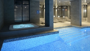 Un área de piscina interior moderna con jacuzzi, sillas de descanso y suelo de baldosas.