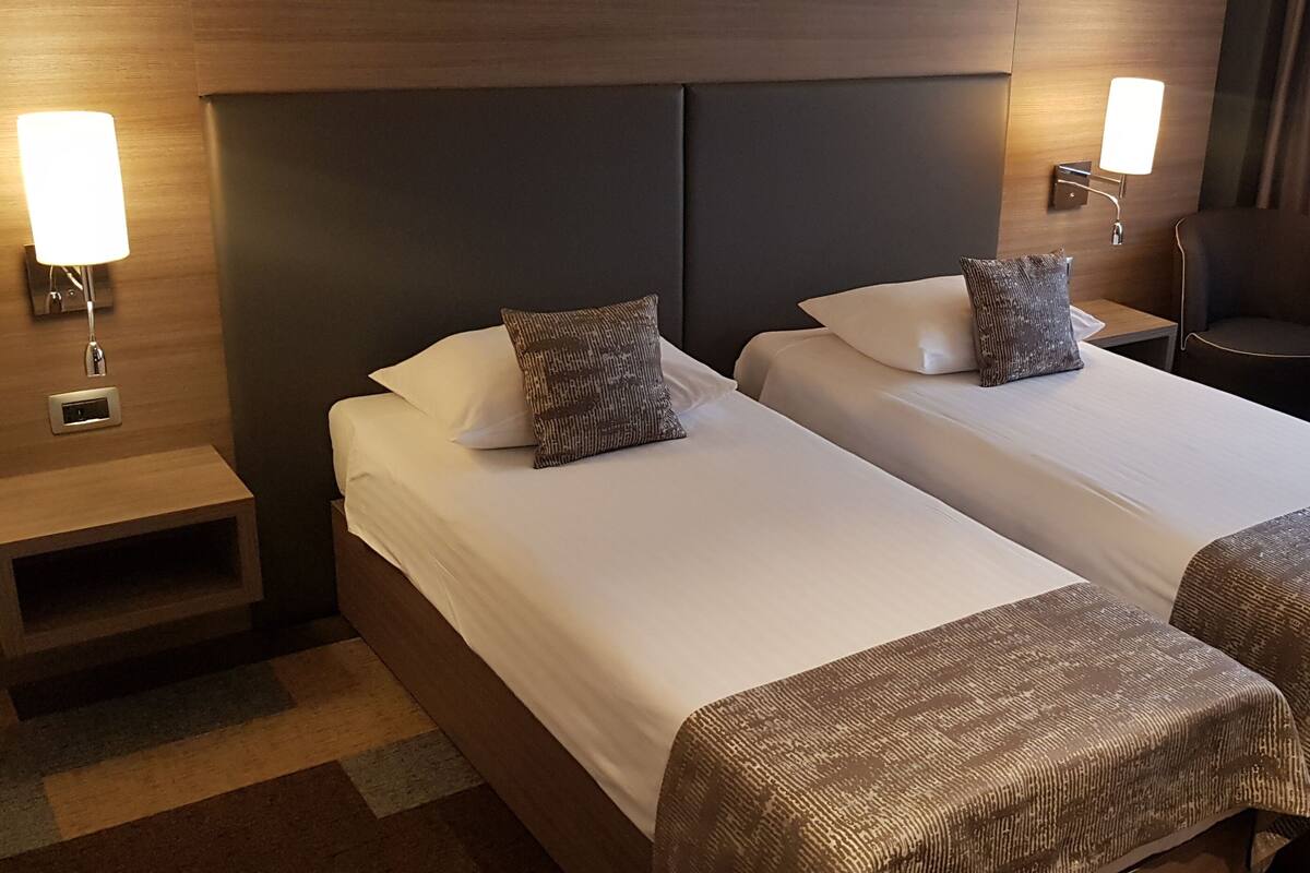 A hotel room with two beds, nightstands, a chair, and a small table.