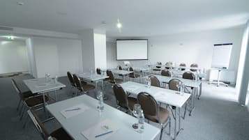 Un salón de conferencias con mesas blancas, sillas marrones y una pantalla para proyector.