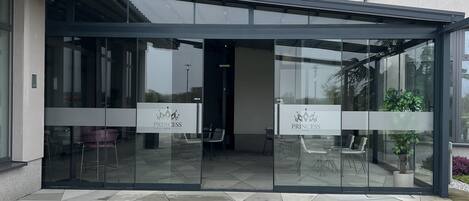 Una entrada de hotel moderna con fachada de vidrio, asientos al aire libre y un patio con baldosas.