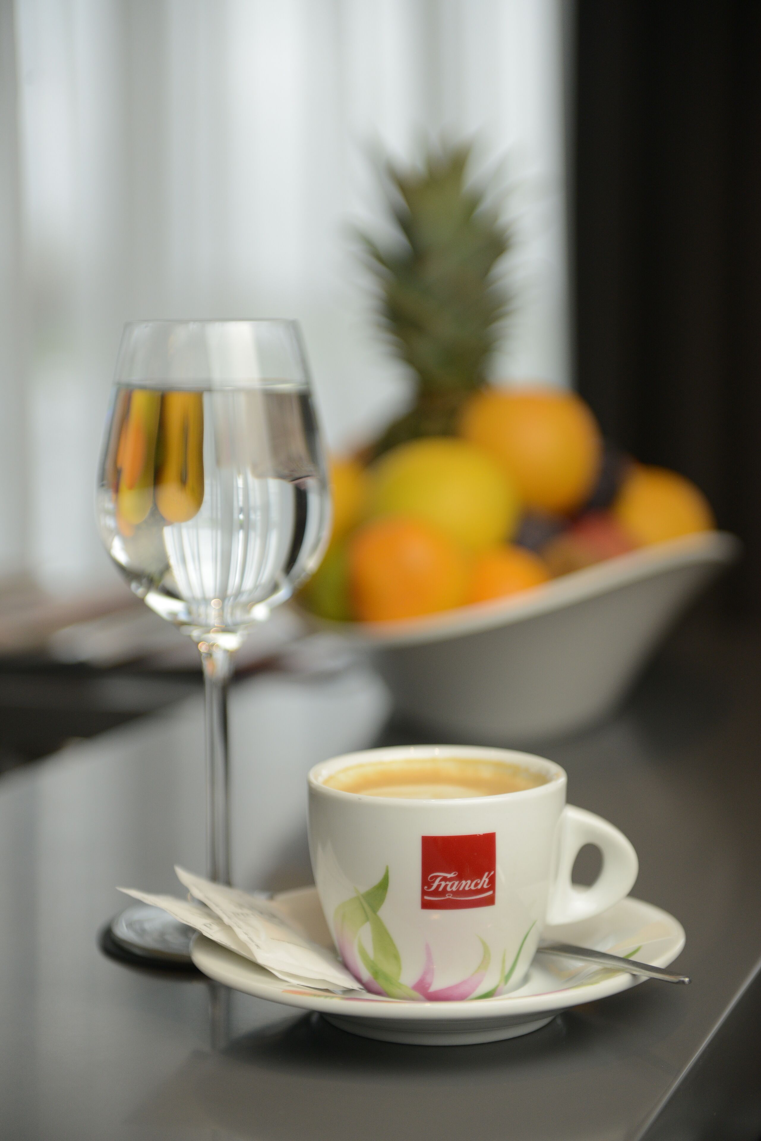 A cup of coffee with a logo, a glass of water, and a bowl of fruit on a table.
