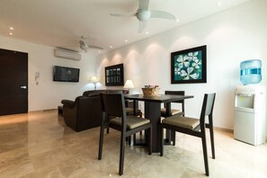 A modern living room with a dining table, chairs, a sofa, a ceiling fan, a TV, and a water dispenser. - Papaya 20 by CocoBR (Playa del Carmen)