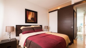 A modern bedroom with a large bed, dark headboard, and a painting above it. - Papaya 20 by CocoBR (Playa del Carmen)