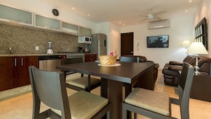 A modern kitchen with granite countertops, a dining area with a dark table and chairs, and a living area with a sofa and a TV. - Papaya 20 by CocoBR (Playa del Carmen)