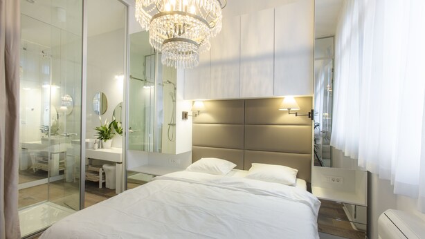 A modern bedroom with a large bed, a glass shower enclosure, a bedside table, and a chandelier. - Ah Design Apartments (Opatija)