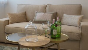 A living room with a beige sofa, a round wooden coffee table, and two bottles of alcohol. - Ah Design Apartments (Opatija)