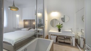 A modern bedroom with a large bed, a glass-enclosed shower, and a white bathroom with a sink and mirror. - Ah Design Apartments (Opatija)