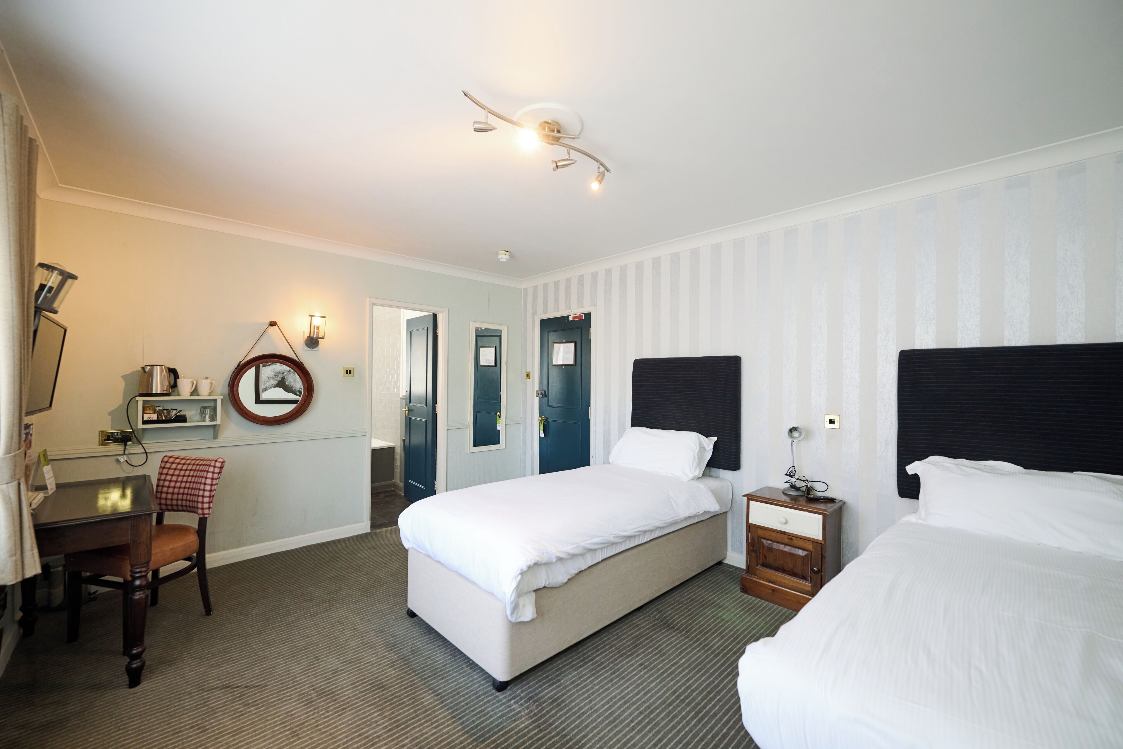 Una camera d'hotel con un letto, una scrivania, una sedia, un tavolino e una mensola a parete.